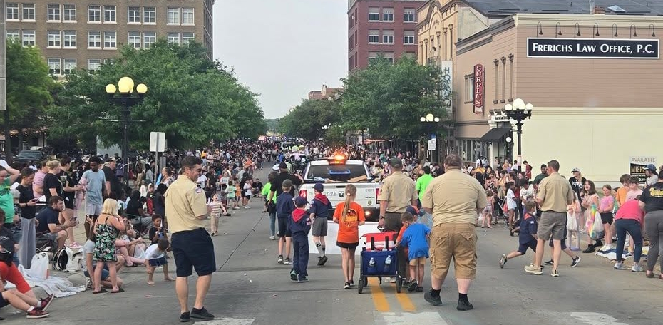 Children marching in a community parade with flags and instruments